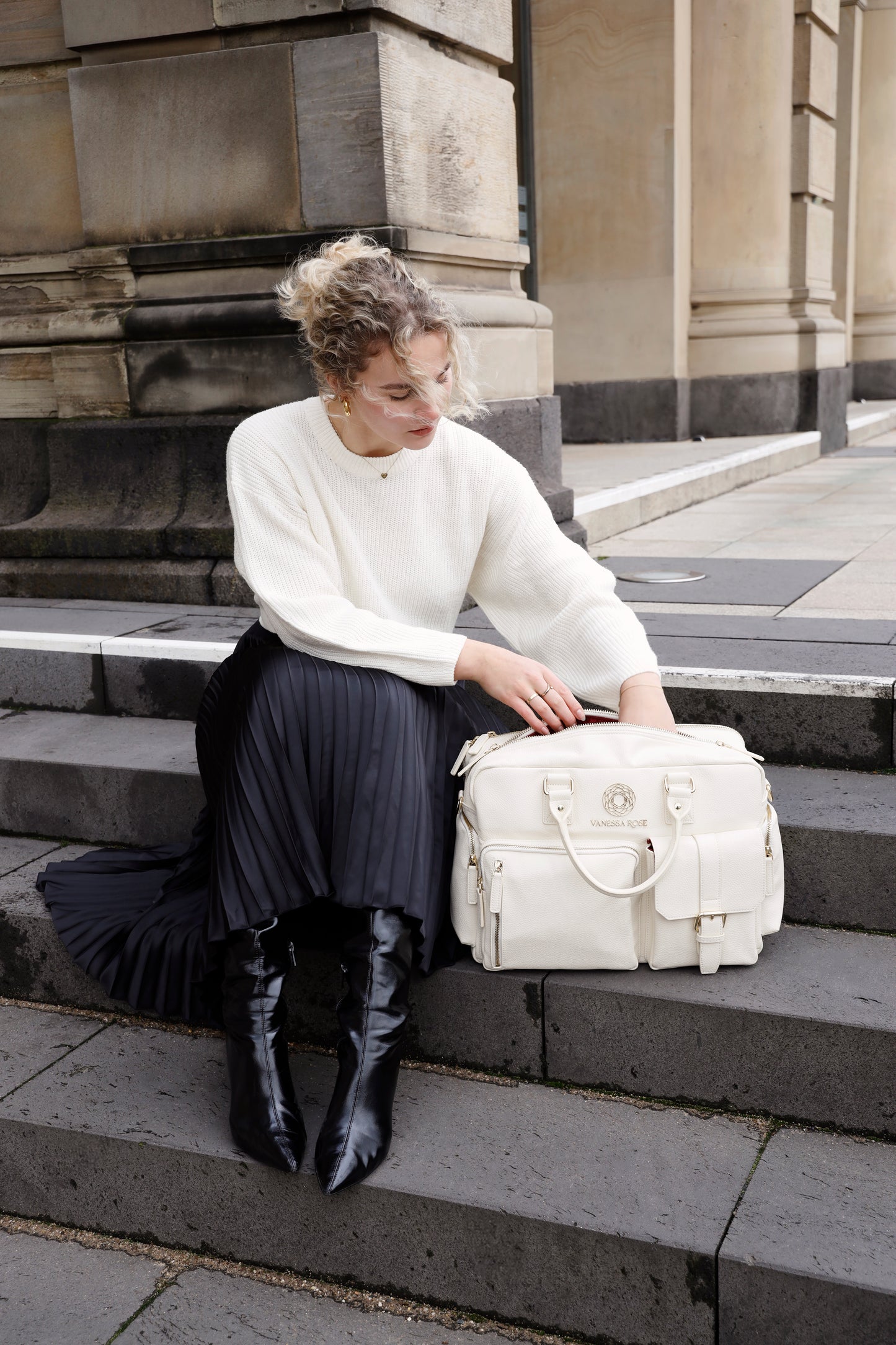 Frau sitzt mit ihrer Kameratasche Aurora in weiß auf einer Treppe