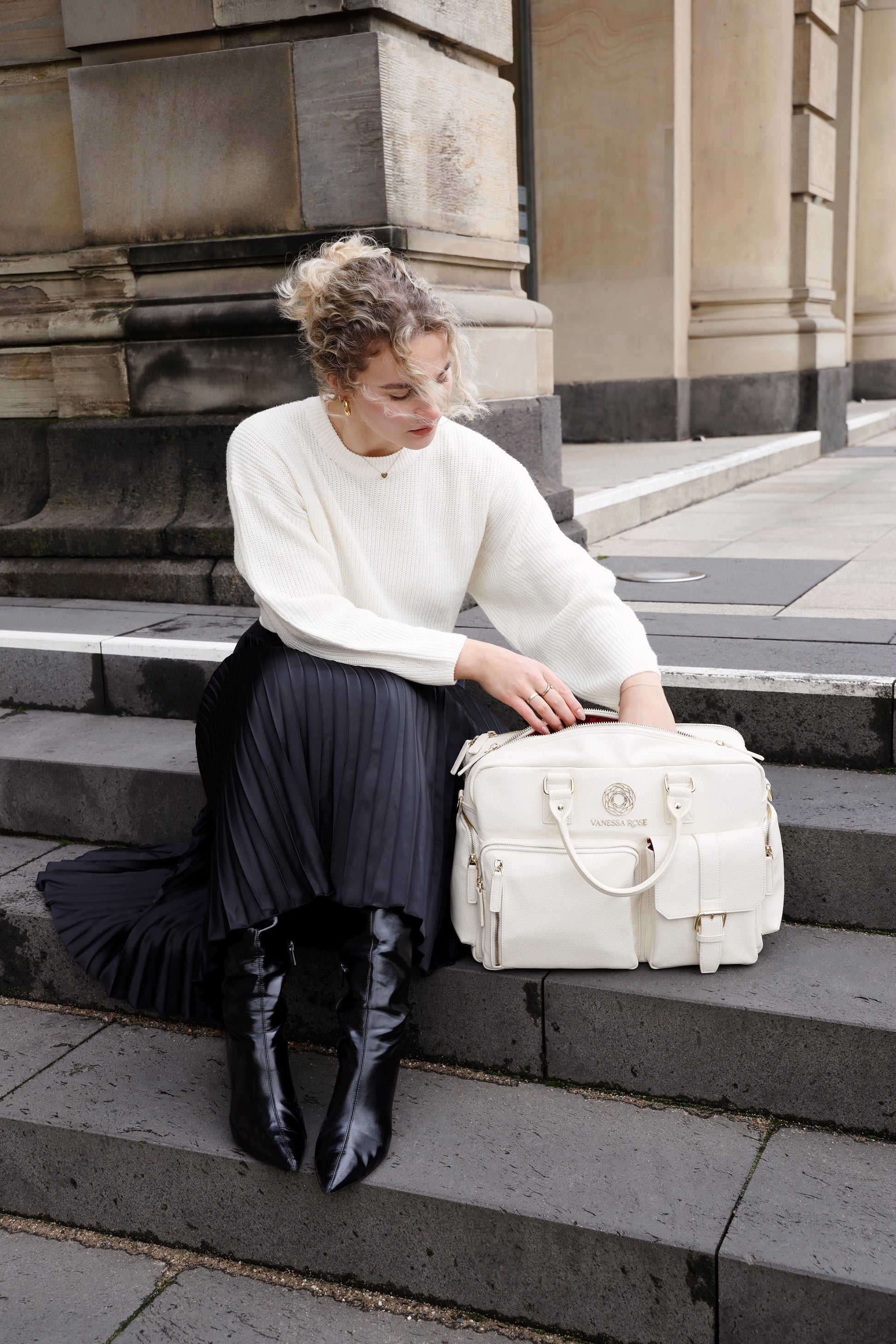 Frau sitzt mit ihrer Kameratasche Aurora in weiß auf einer Treppe